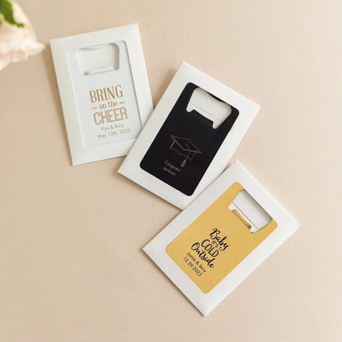 Three personalized bottle openers in packaging on a beige background