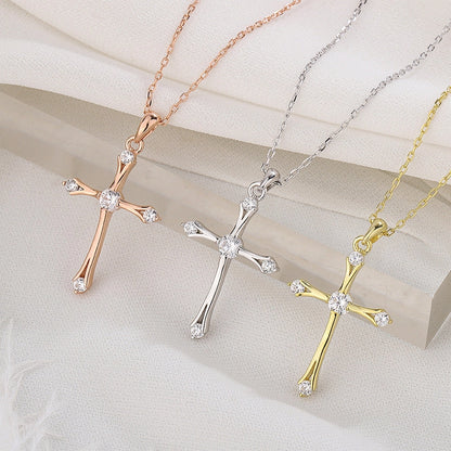 Three cross-shaped pendants in rose gold, silver, and gold on a light background