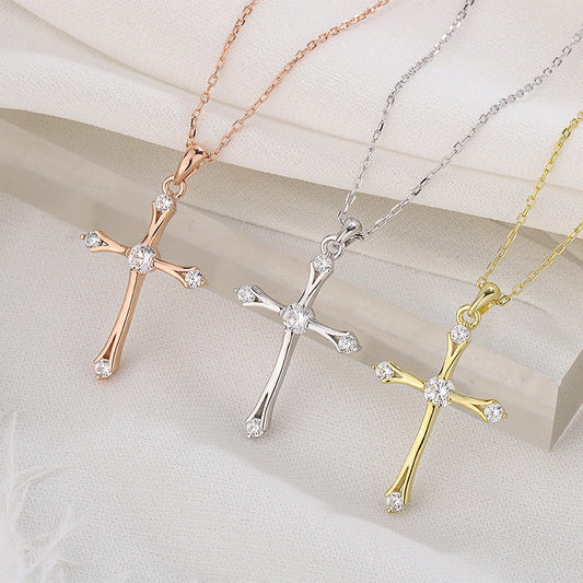 Three cross-shaped pendants in rose gold, silver, and gold on a light background