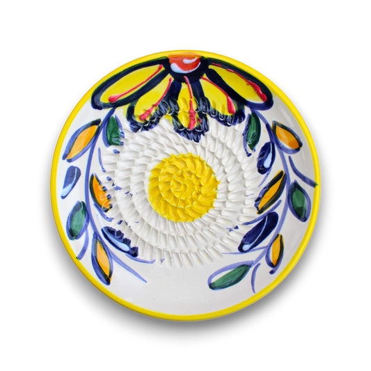 A round white ceramic plate with a hand-painted Talavera style floral design, featuring a yellow center, yellow and orange petals with blue outlines, and blue and green leaves around the rim.