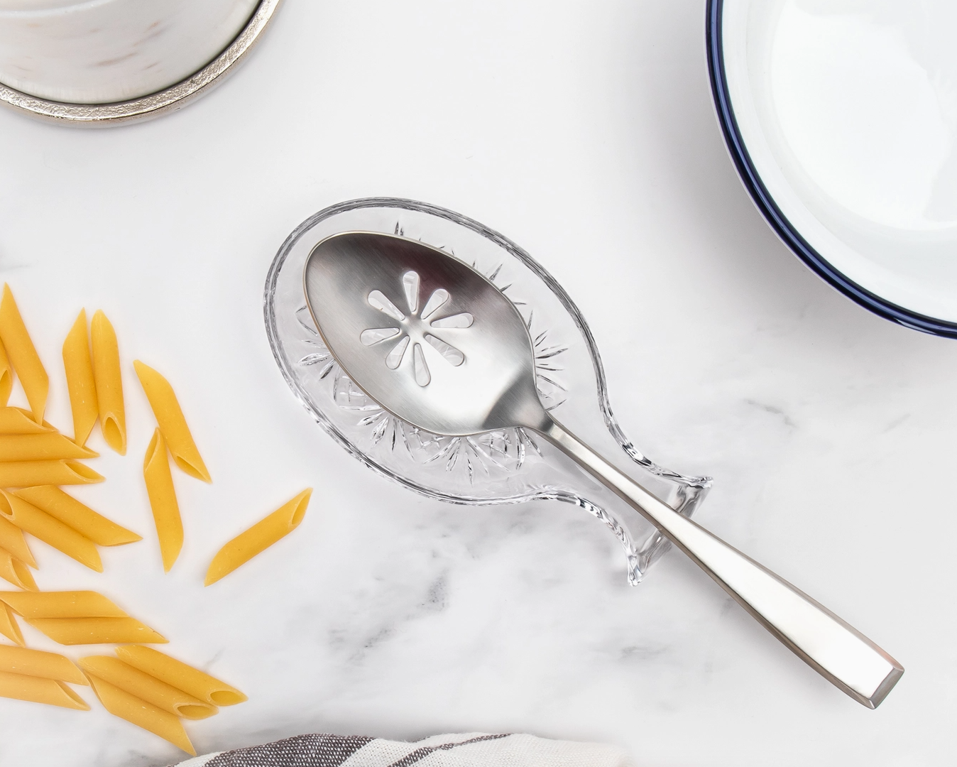 Decorative silver spoon with floral design on a marble surface with penne pasta.