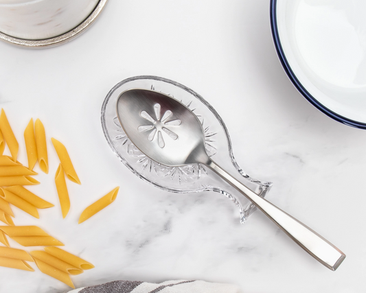 Decorative silver spoon with floral design on a marble surface with penne pasta.
