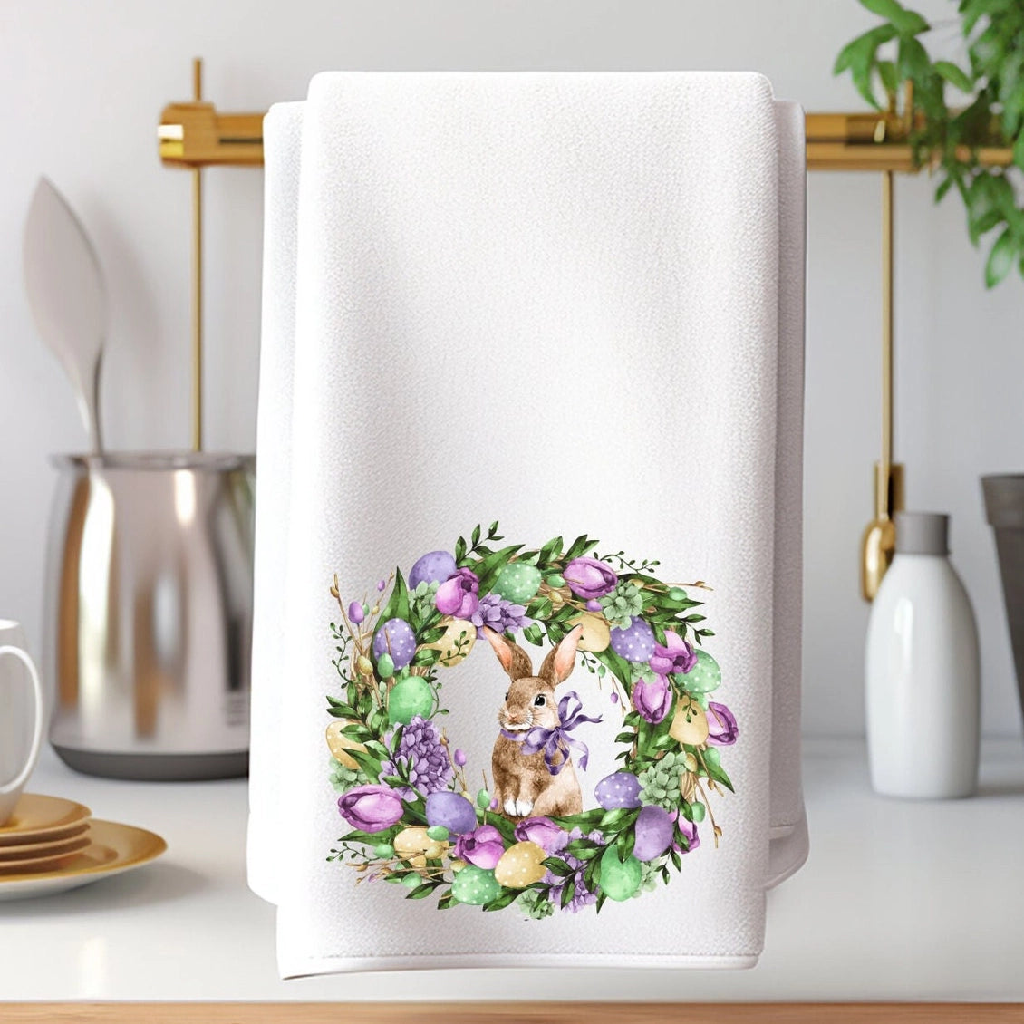 White towel with a decorative wreath design featuring bunnies and flowers on a kitchen counter.