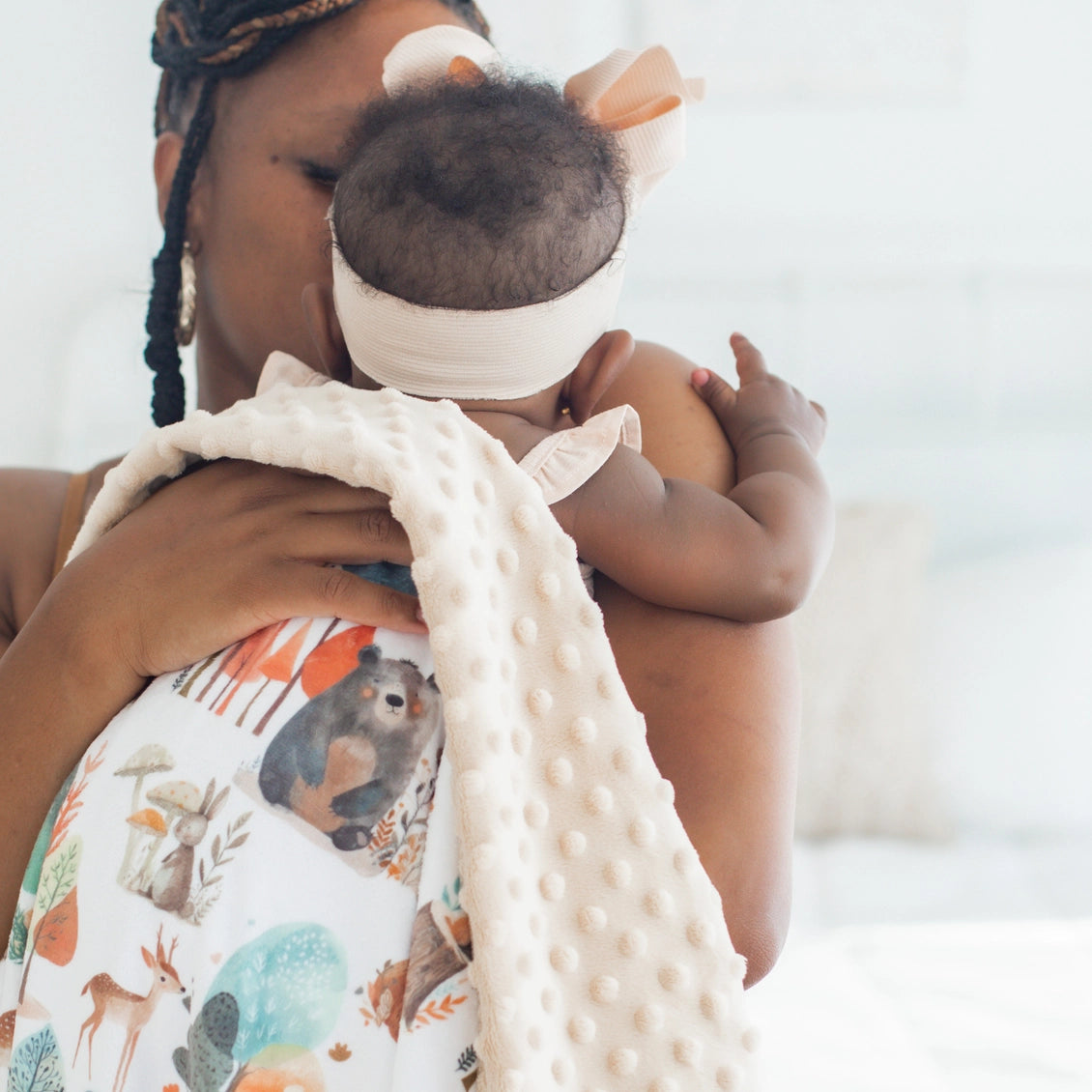 Woman holding a baby wrapped in a blanket with animal prints against a blurred background