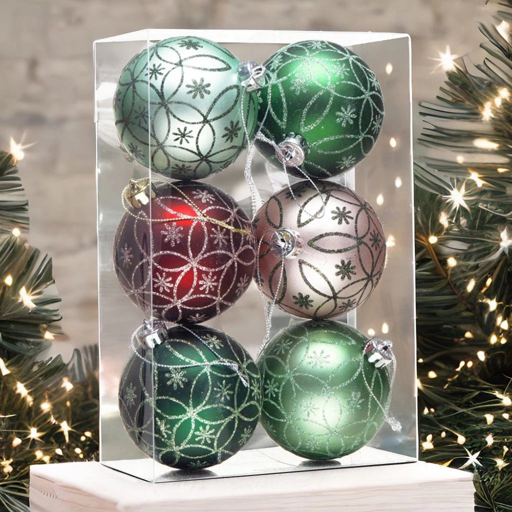 Set of green and red Christmas ornaments in a clear box with a blurred Christmas tree background.