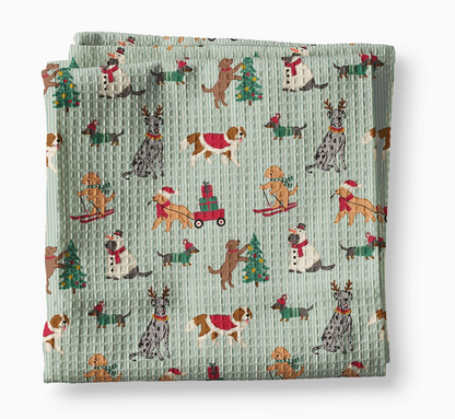 Festive Christmas dog waffle weave kitchen towel with illustrated dogs decorating trees, skiing, pulling presents and wearing holiday outfits on a blue striped background.