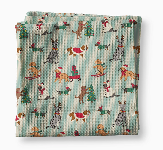 Festive Christmas dog waffle weave kitchen towel with illustrated dogs decorating trees, skiing, pulling presents and wearing holiday outfits on a blue striped background.