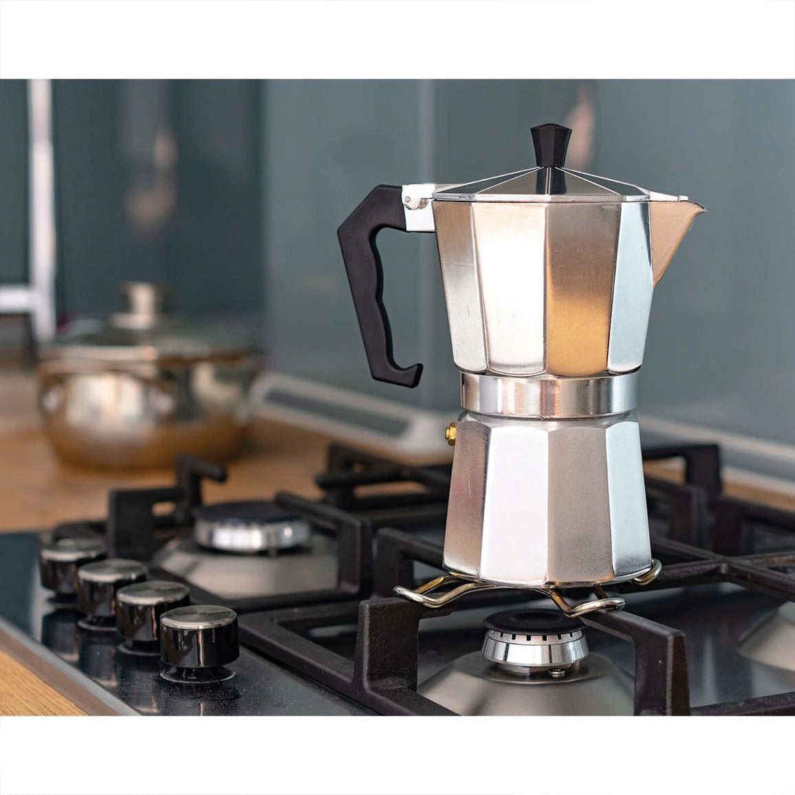 Stainless steel Moka pot on a gas stove with a blurred kitchen background