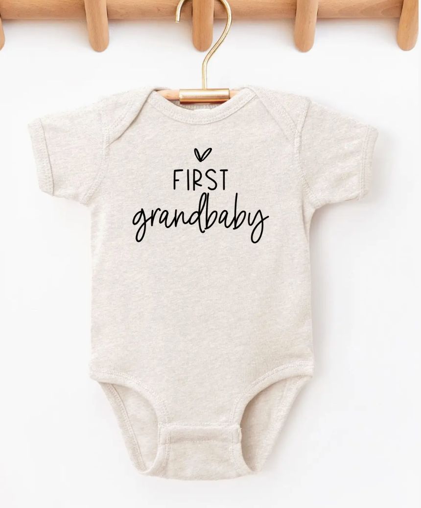 Beige baby onesie with 'First grandbaby' text on a white background