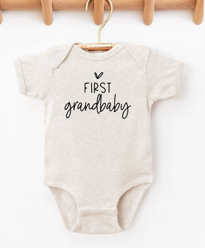 Beige baby onesie with 'First grandbaby' text on a white background