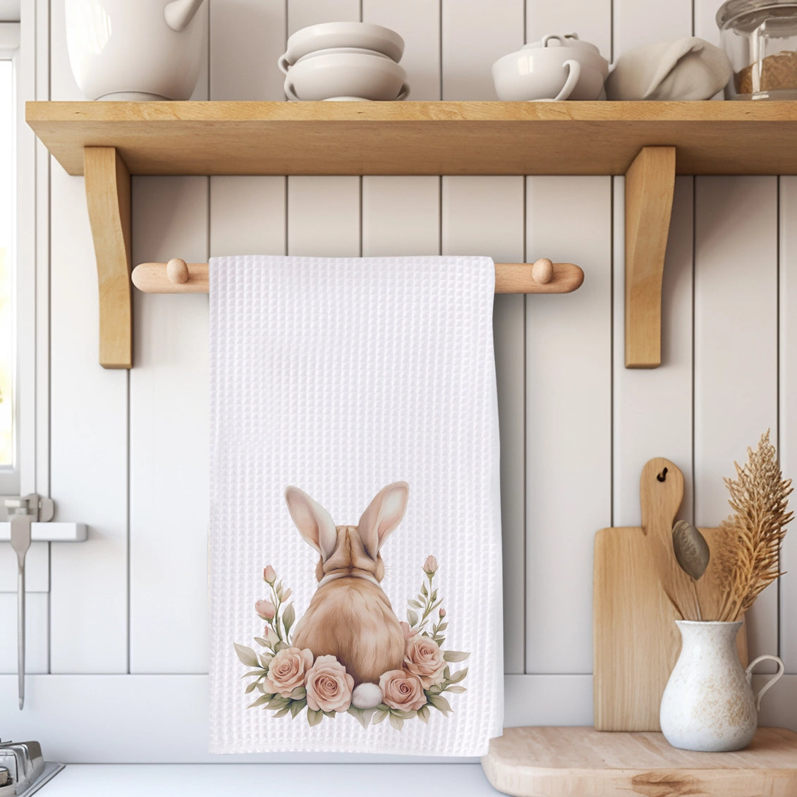 Kitchen towel with a bunny design hanging on a wooden rack, with kitchen utensils and decor in the background.