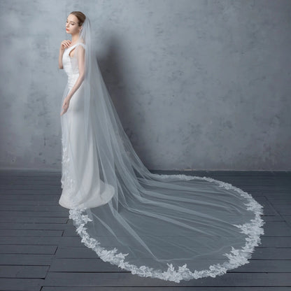 Woman wearing a white wedding dress with a long veil against a gray background
