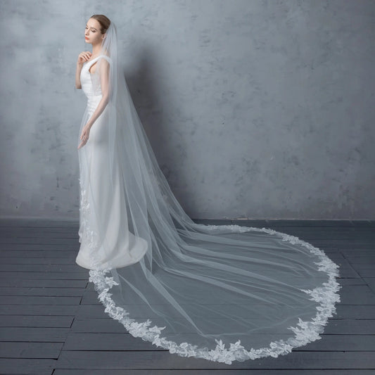 Woman wearing a white wedding dress with a long veil against a gray background
