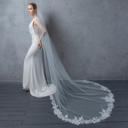Woman in a white wedding dress with a long veil against a gray background