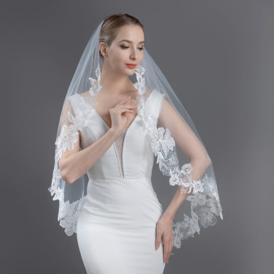 Woman wearing a white wedding dress with a lace veil against a gray background