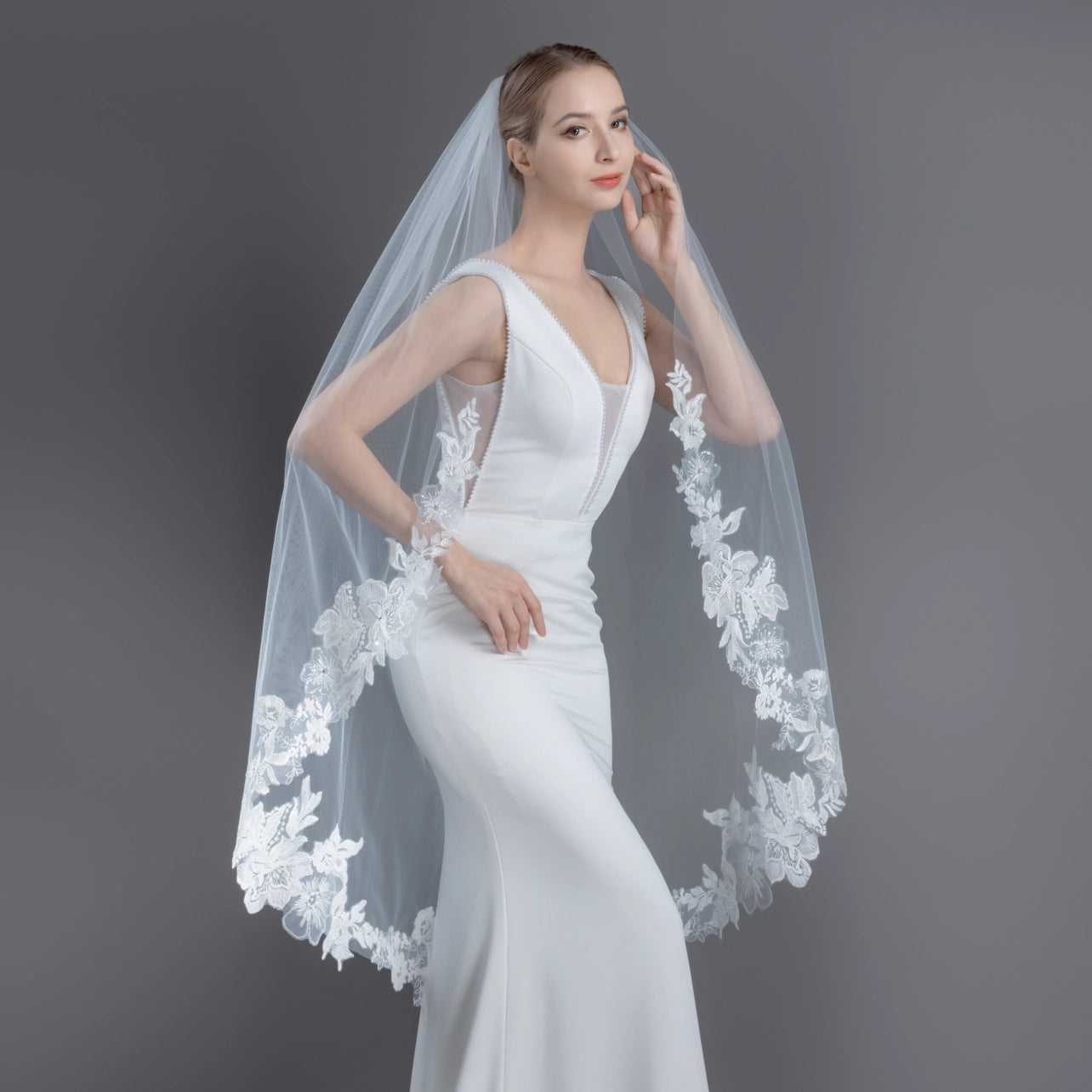 Woman wearing a white wedding dress with a floral veil against a gray background