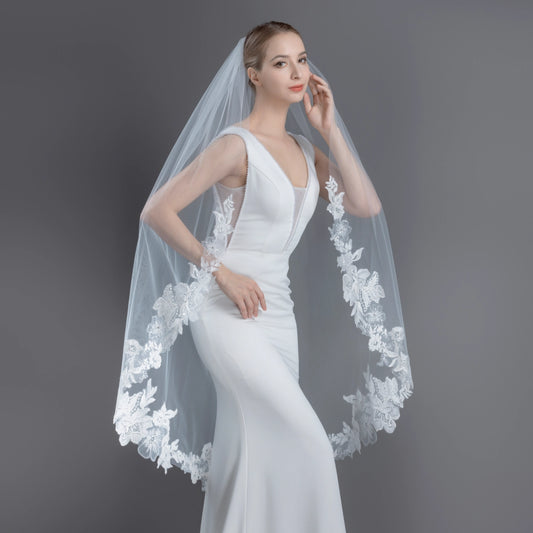 Woman wearing a white wedding dress with a floral veil against a gray background