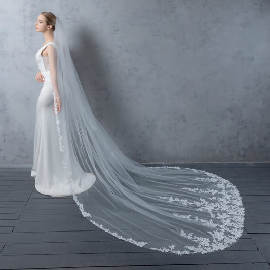 Bride in a white wedding dress with a long, elegant veil against a gray background