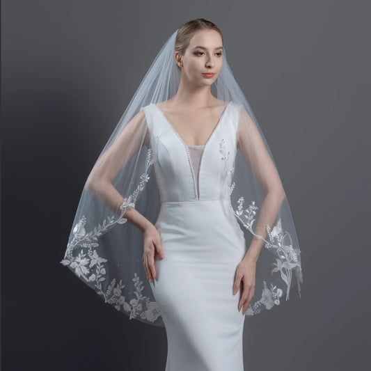 Woman wearing a white wedding dress with an embroidered veil against a dark background