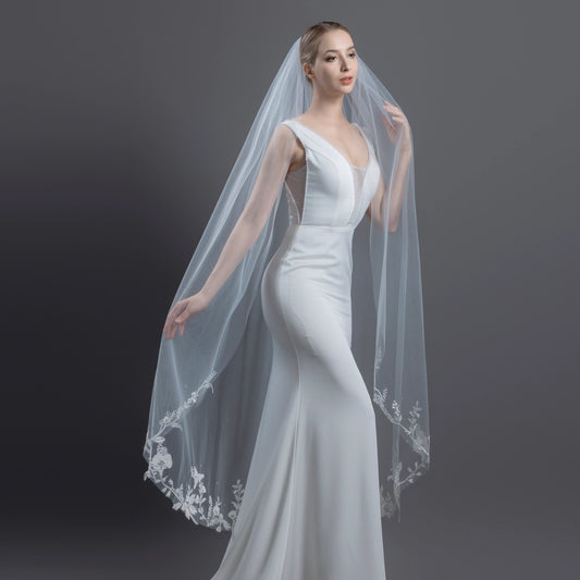 Woman wearing a white wedding dress with a long veil against a dark background