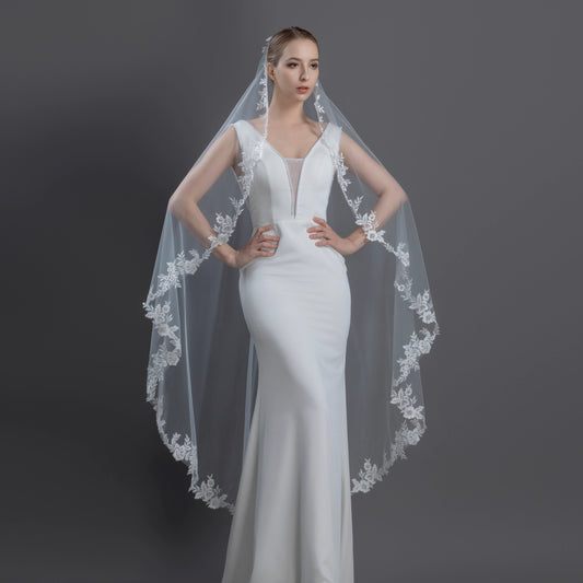 Woman wearing an ivory mantilla wedding dress with a long veil on a dark background