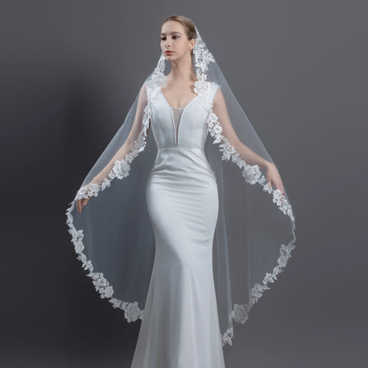 Woman wearing a white wedding dress with an intricate lace veil against a dark background