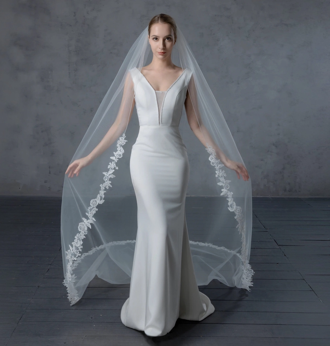 Woman wearing a white wedding dress with a long veil against a gray background