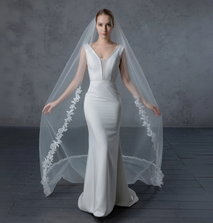 Woman wearing a white wedding dress with a long veil against a gray background