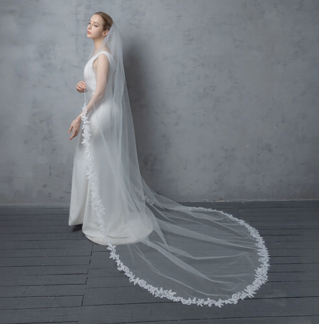 Woman wearing a white wedding dress with a long veil against a gray background