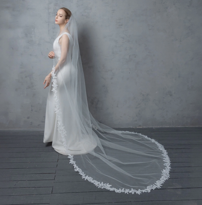 Woman wearing a white wedding dress with a long veil against a gray background