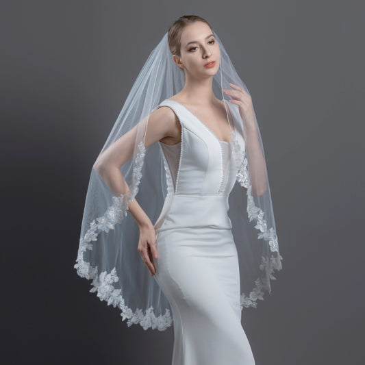 Woman wearing a white wedding dress with a lace veil against a gray background