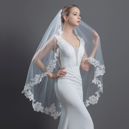 Woman wearing a white wedding dress with a lace veil against a dark background