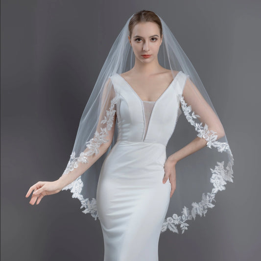 Woman wearing a white wedding dress with a lace veil against a dark background