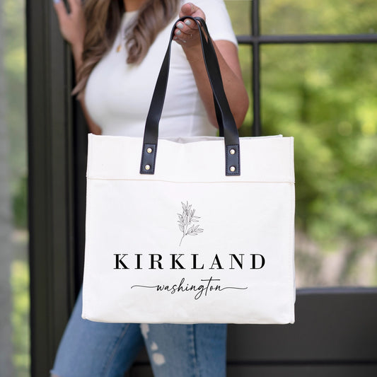 White tote bag with 'Kirkland, Washington' text held by a person outdoors.