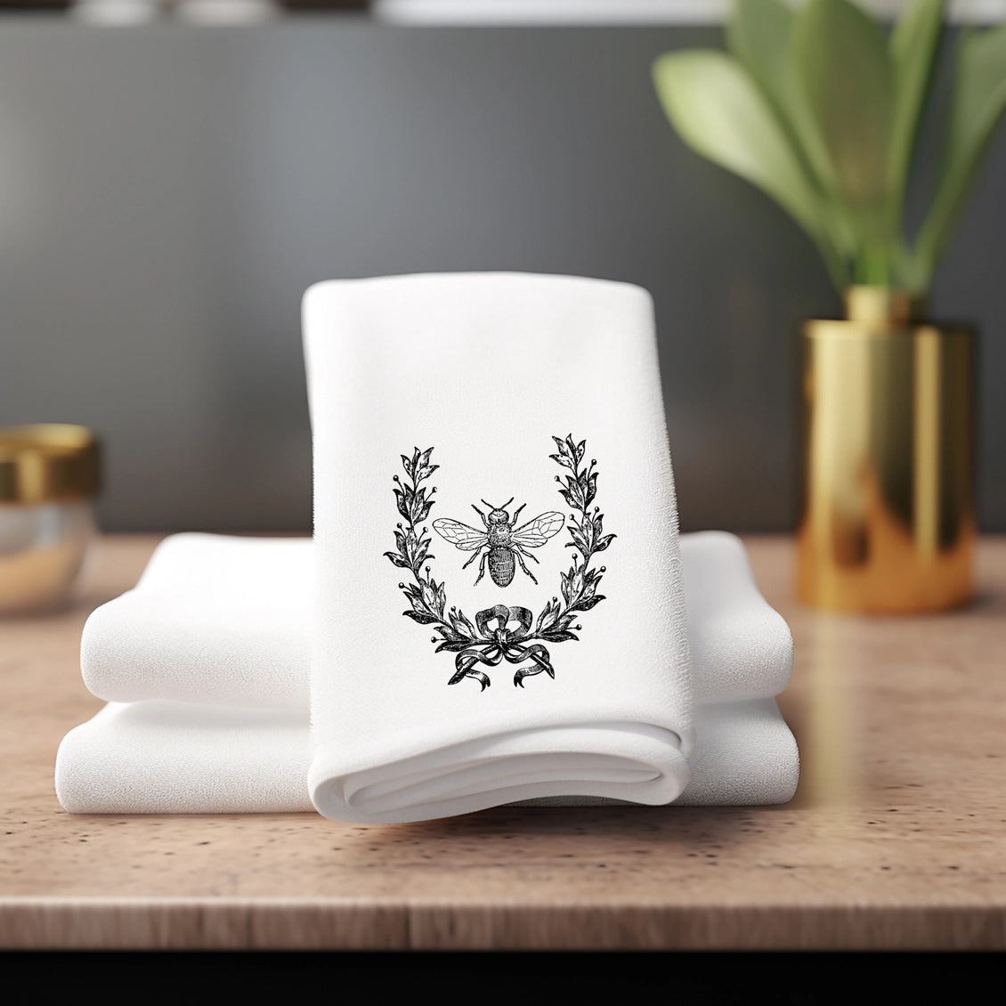 White towels with a black bee and wreath design on a wooden surface.