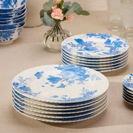Set of blue and white floral-patterned plates on a beige surface with a vase of flowers in the background.
