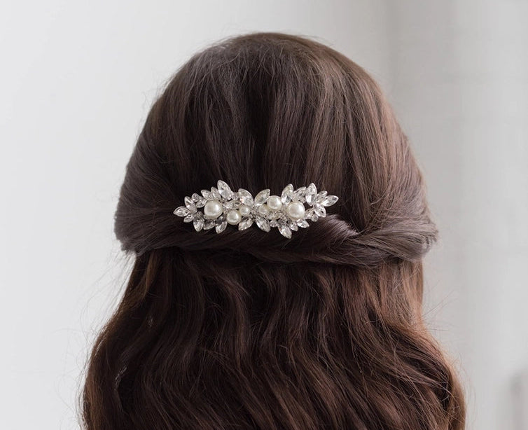 Person with long, wavy hair wearing a decorative hair clip against a plain background