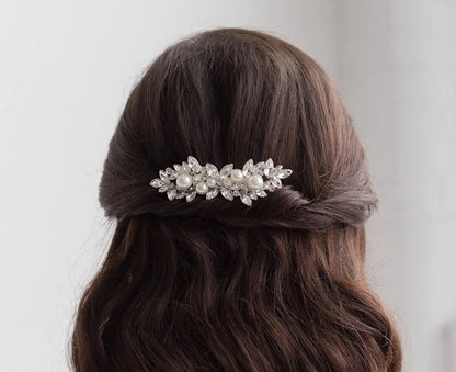 Person with long, wavy hair wearing a decorative hair clip against a plain background