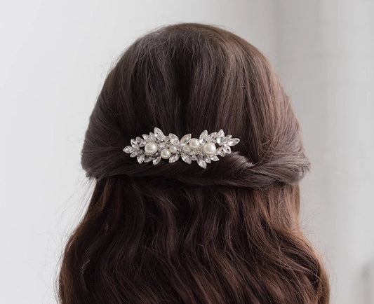 Person with long, wavy hair wearing a decorative hair clip against a plain background