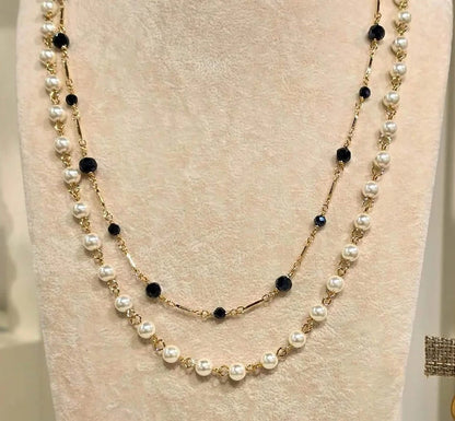 A double-strand pearl and gold necklace displayed on a cream jewelry bust, with matching drop earrings on a textured stand beside it.
