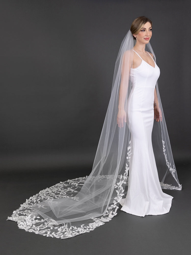 Woman wearing a white wedding dress with a long, lace-trimmed veil against a dark background