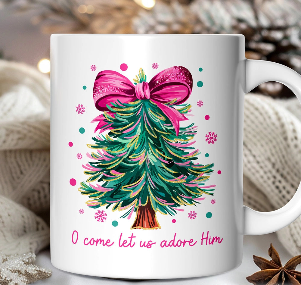 White mug with Christmas tree design and pink bow, featuring text 'O come let us adore Him' on a blurred background.