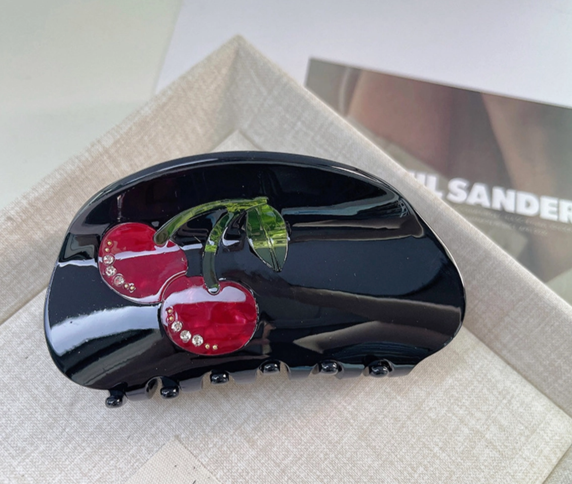 Black hair clip with red cherry design on a light gray surface