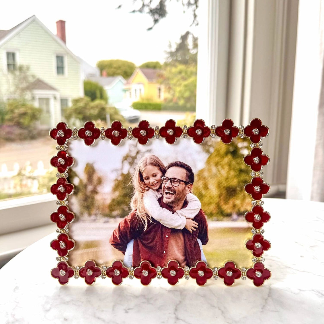 Decorative photo frame with red floral design on a surface with a blurred outdoor background
