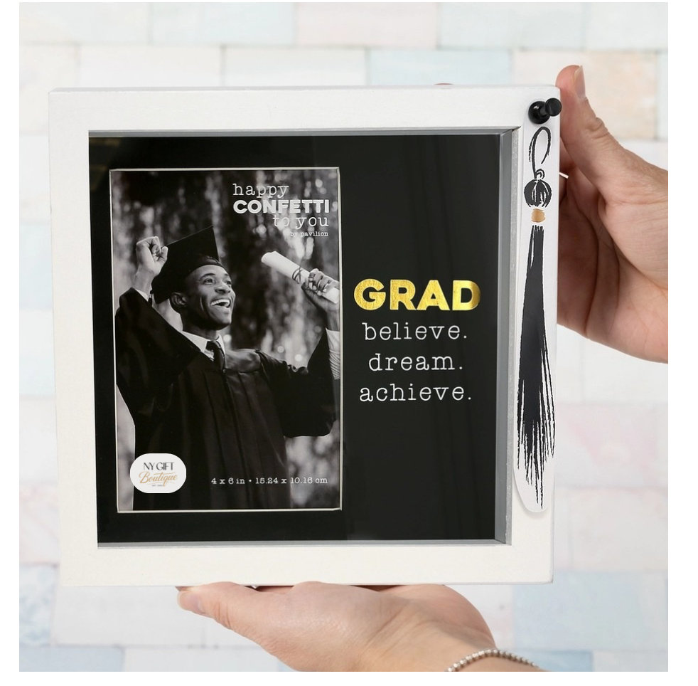 Graduation-themed photo frame with tassel, held by a hand against a light-colored wall.