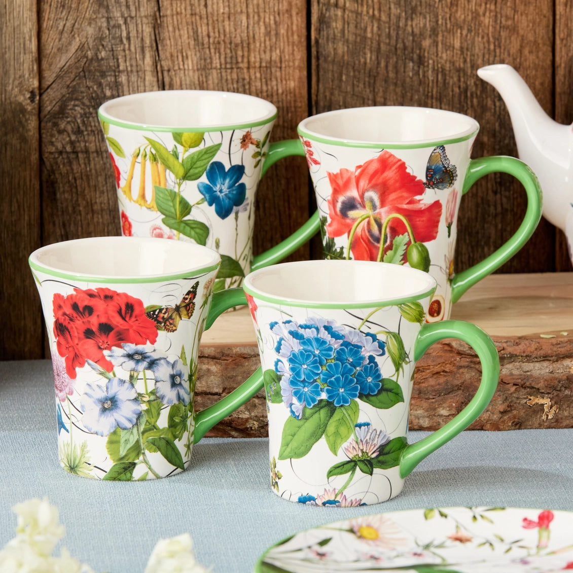 Set of four floral mugs with green handles on a wooden surface.