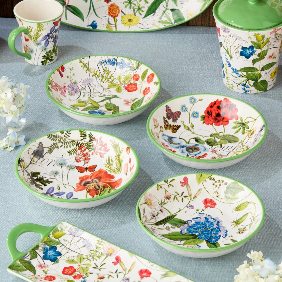 Set of floral-patterned bowls and mugs on a blue surface with white flowers.