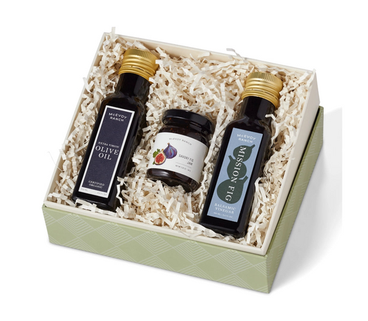 Two bottles of olive oil and a jar of balsamic vinegar in a gift box on a white background