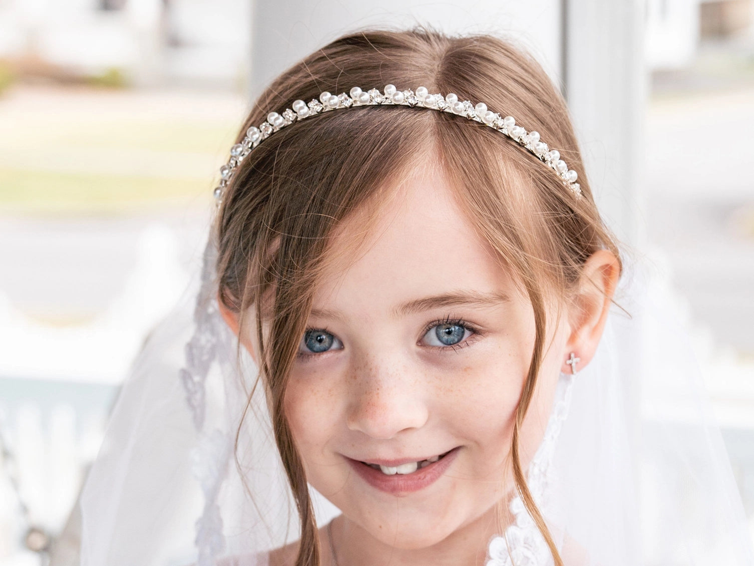 Young girl wearing a pearl headband and veil, smiling.