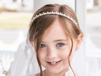 Young girl wearing a pearl headband and veil, smiling.